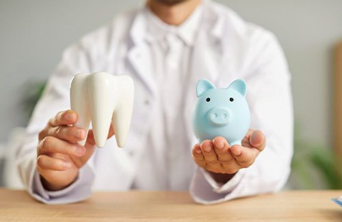 A dentist holding up a large model tooth and a light blue piggy bank