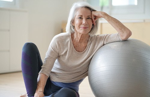 Senior woman smiling while resting against balance ball