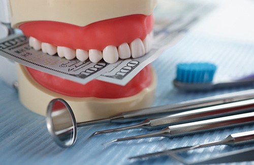 A jaw mockup biting some dollar bills next to dental tools