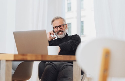 Man with glasses smiling while working on laptop