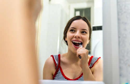 Patient in Orem brushing teeth carefully around traditional braces