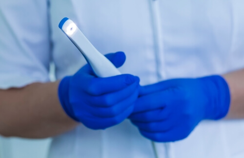 Gloved hands holding a thin white intraoral camera