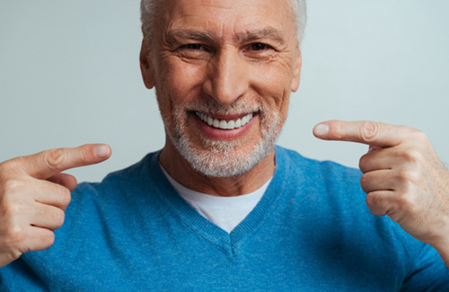 A handsome older man pointing to his new dentures