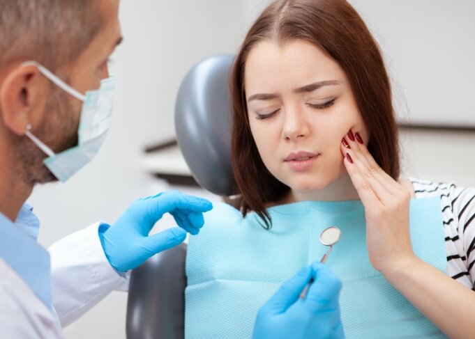 Woman holding her cheek in pain while talking to emergency dentist in Orem