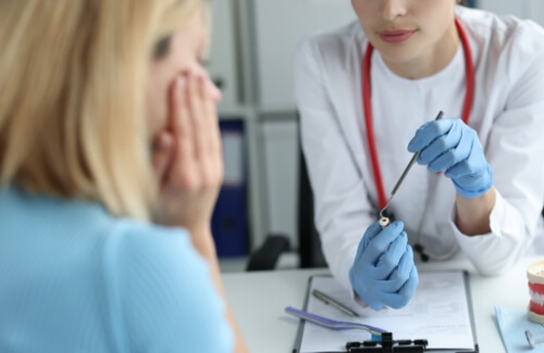 Dentist sitting at desk with patient showing them a tooth model