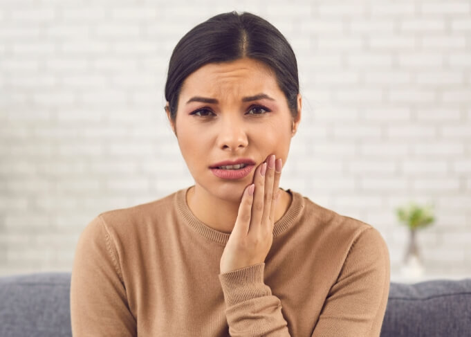 Woman in brown sweater holding her jaw in pain before tooth extractions in Orem