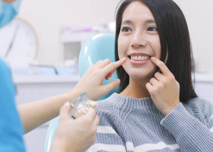 Woman in dental chair pointing to her smile with dental implants in Orem
