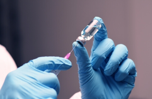 Gloved hands drawing syringe from vial of clear liquid