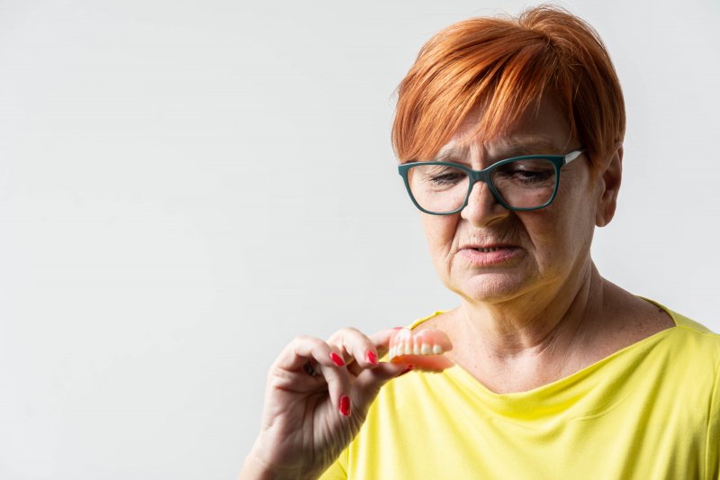 A dissatisfied older woman holding a denture in her hand