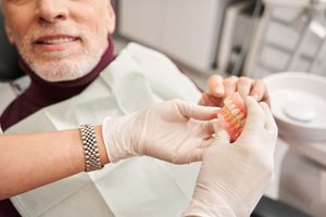 Gloved hands handing dentures to man in dental chair